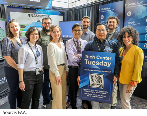 A group of eight men and women standing in front of an exhibit booth. Image Source: FAA.