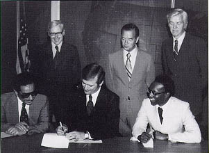 Deputy Administrator Karl S. Bowers signs the United States-Saudi Arabian Highway Development Technical Assistance Agreement as Saudi Arabia's Deputy Minister of Communications, Dr. Nasser Al-Salloum (left), awaits his turn to sign. Seated at right is Assistant Secretary for Policy, Plans and International Affairs Chester C. Davenport. Standing, left to right, are William Moser, Deputy Director, Office of Saudi Arabian Affairs, US Department of the Treasury; and FHWA officials Harry Lindberg, Associate Administrator for Engineering and Traffic Operations; and Dr. Gerald D. Love, Associate Administrator for Research and Development.