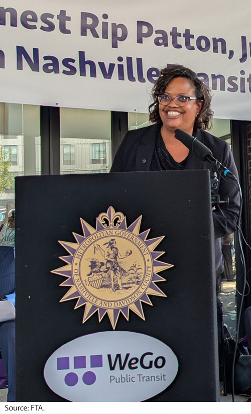 A woman stands at an outdoor podium in front of the Dr. Ernest Rip Patton, Jr North Nashville Transit Center. On the podium is a seal for the Metropolitan Government of Nashville and Davidson County. Image Source: FTA.