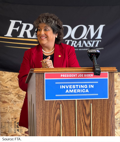 A woman stands at a podium that holds a sign with “Investing in America.” Image Source: FTA.