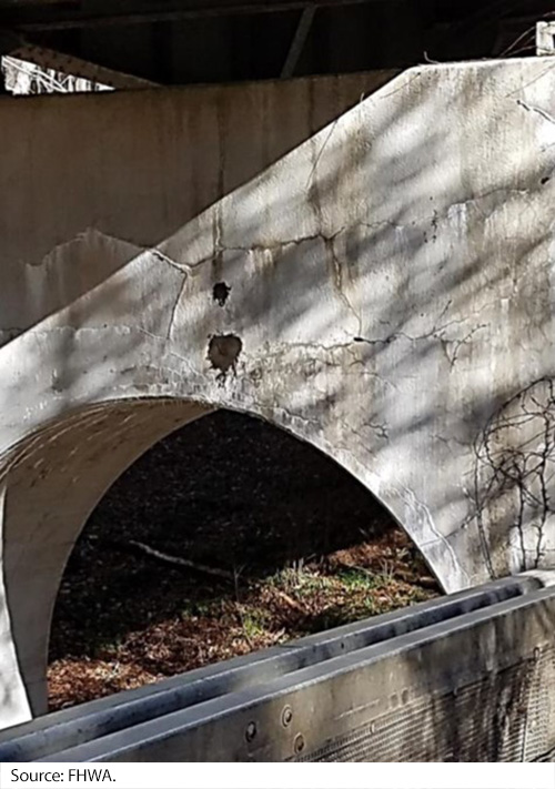 The opening of a tunnel made of concrete. Above the opening are large cracks and chips in the concrete. Image Source: FHWA.