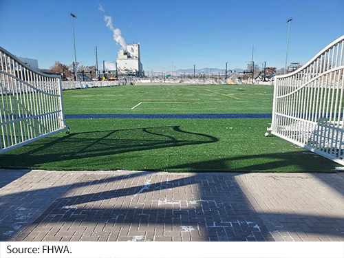 An opened white gate leads to a large artificial turf soccer field. Image Source: FHWA.