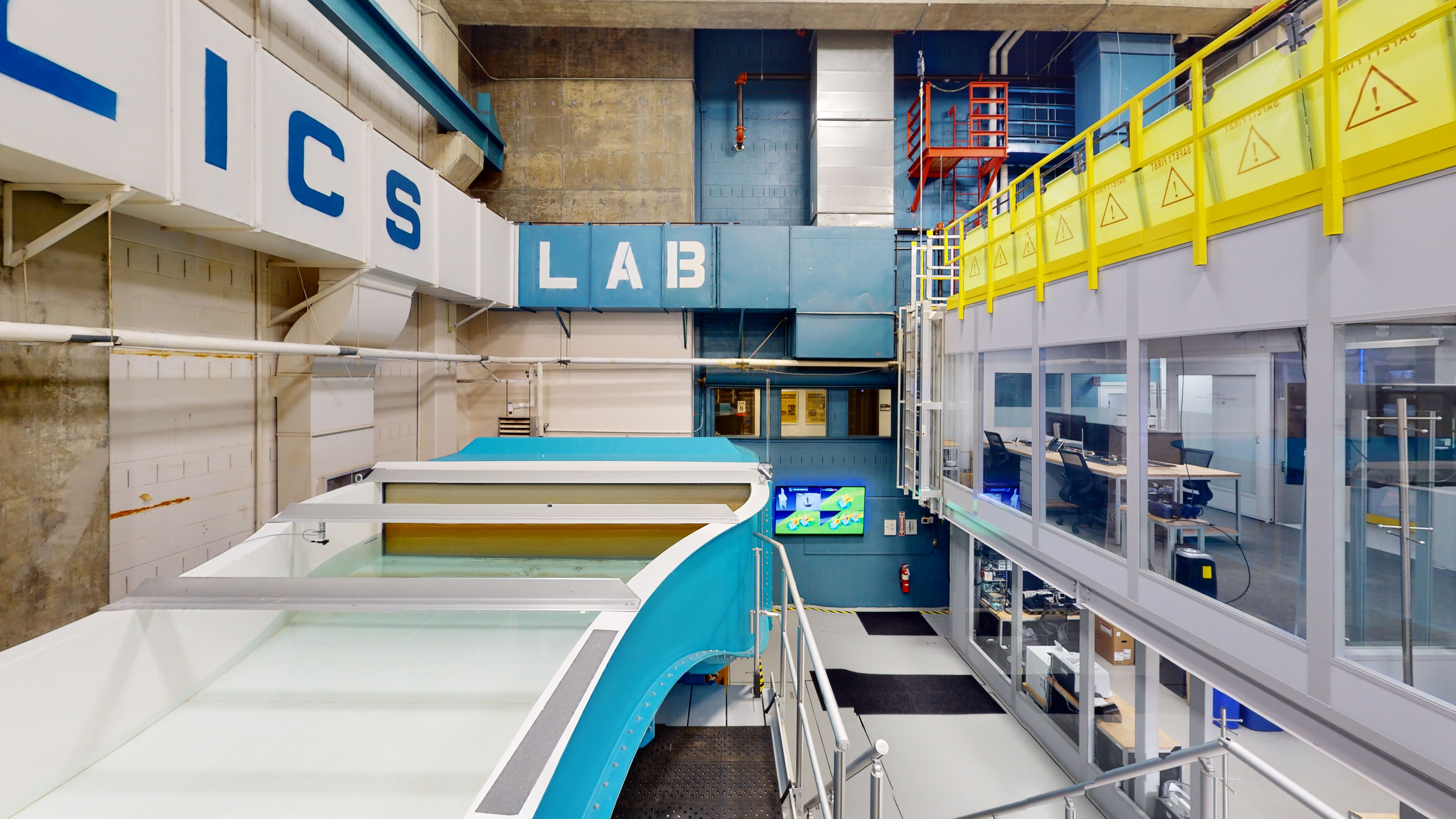 On the left is a large, open basin of the flume system, and on the right are two levels of offices that have desks and computer workstations.  