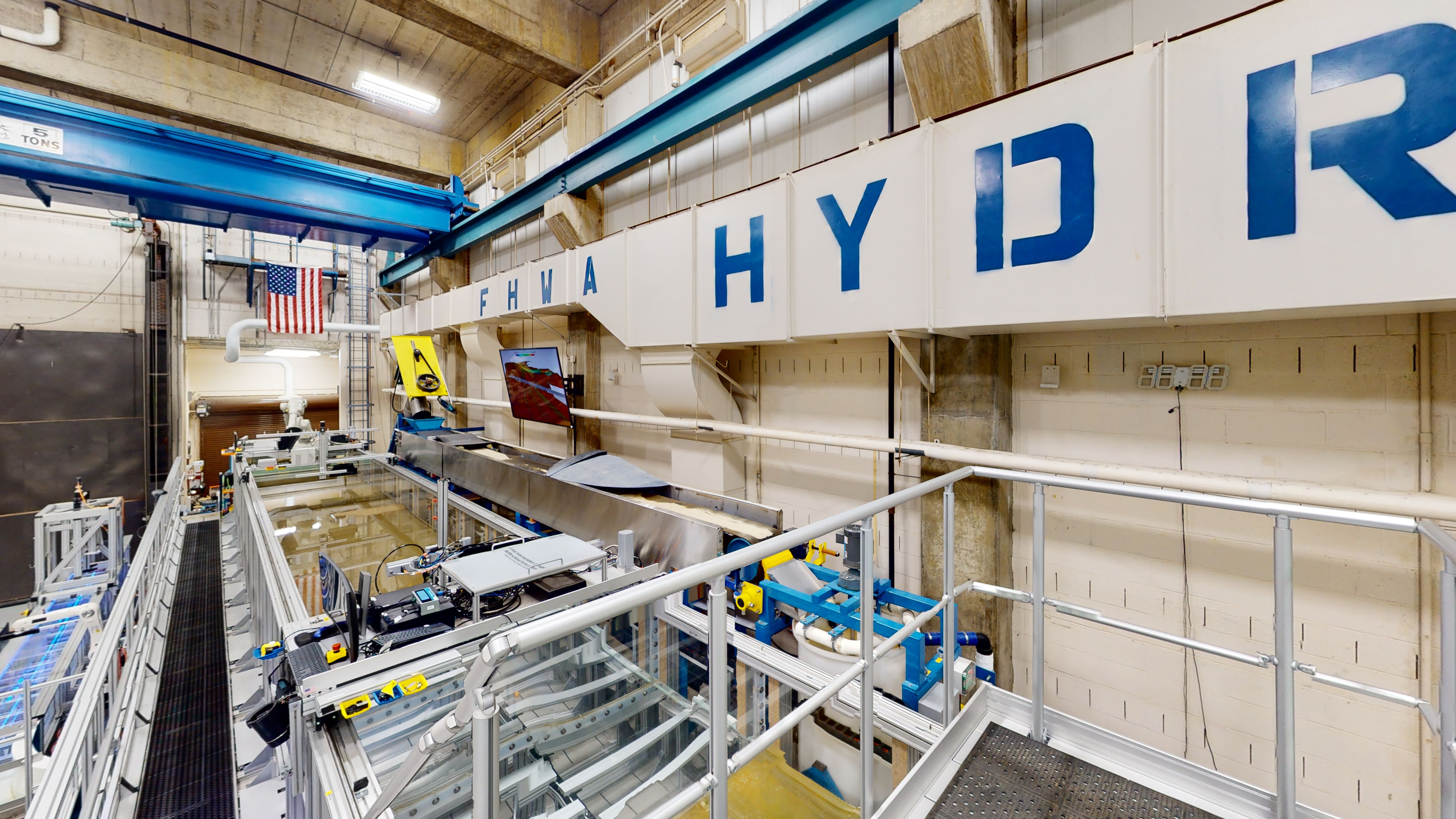 Test section of the flume system with a conveyor belt and robotic arm. Below the conveyor belt is a section with channels and equipment.  