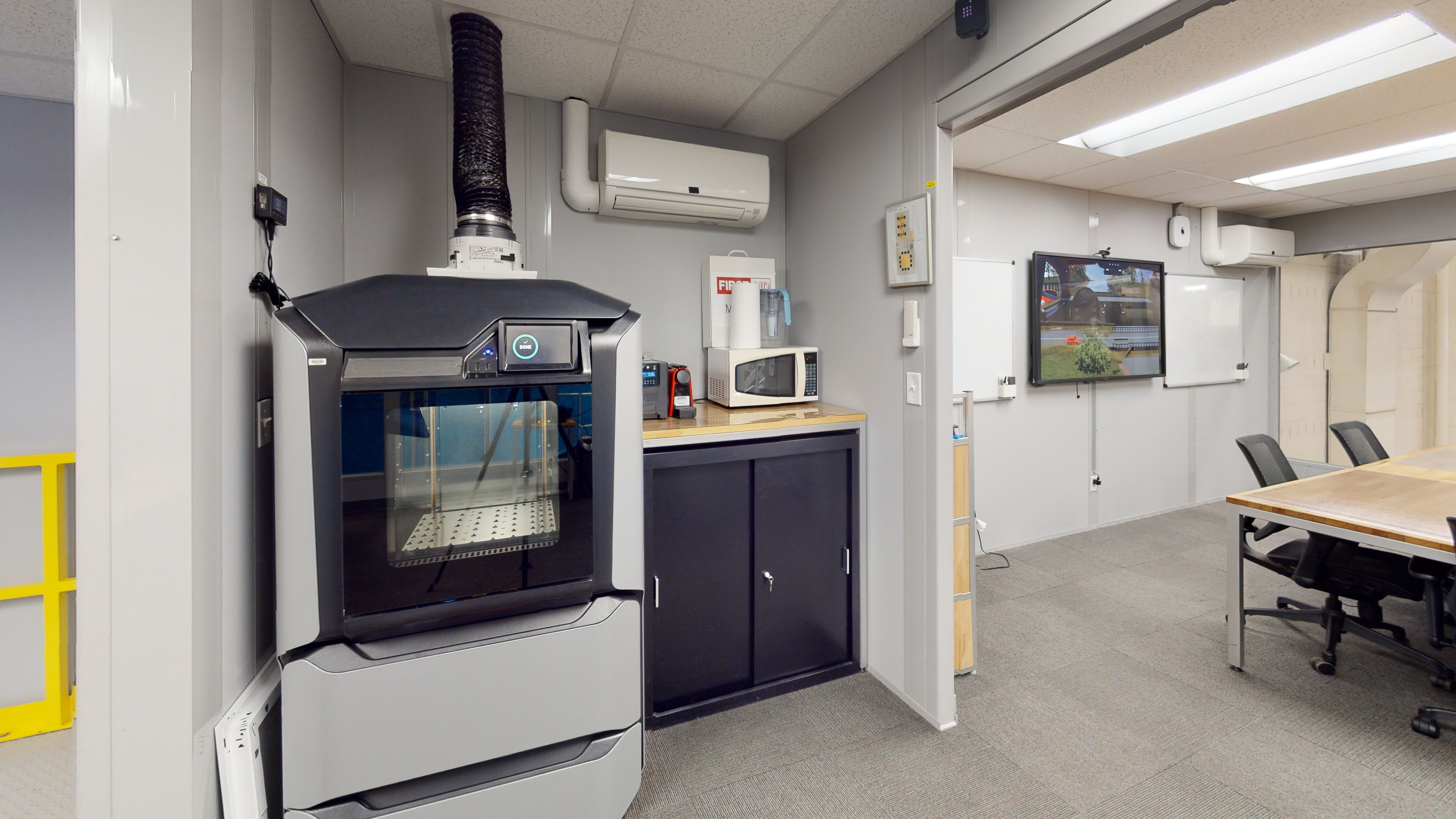 A large three-dimensional printer next to a small cabinet. 