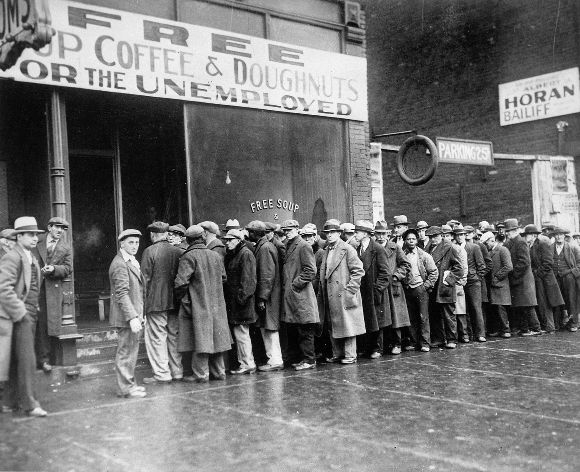 Unemployed men queued outside a depression soup kitchen opened in Chicago preceding Social Security. The storefront sign reads: Free Soup, Coffee and Doughnuts for the Unemployed.