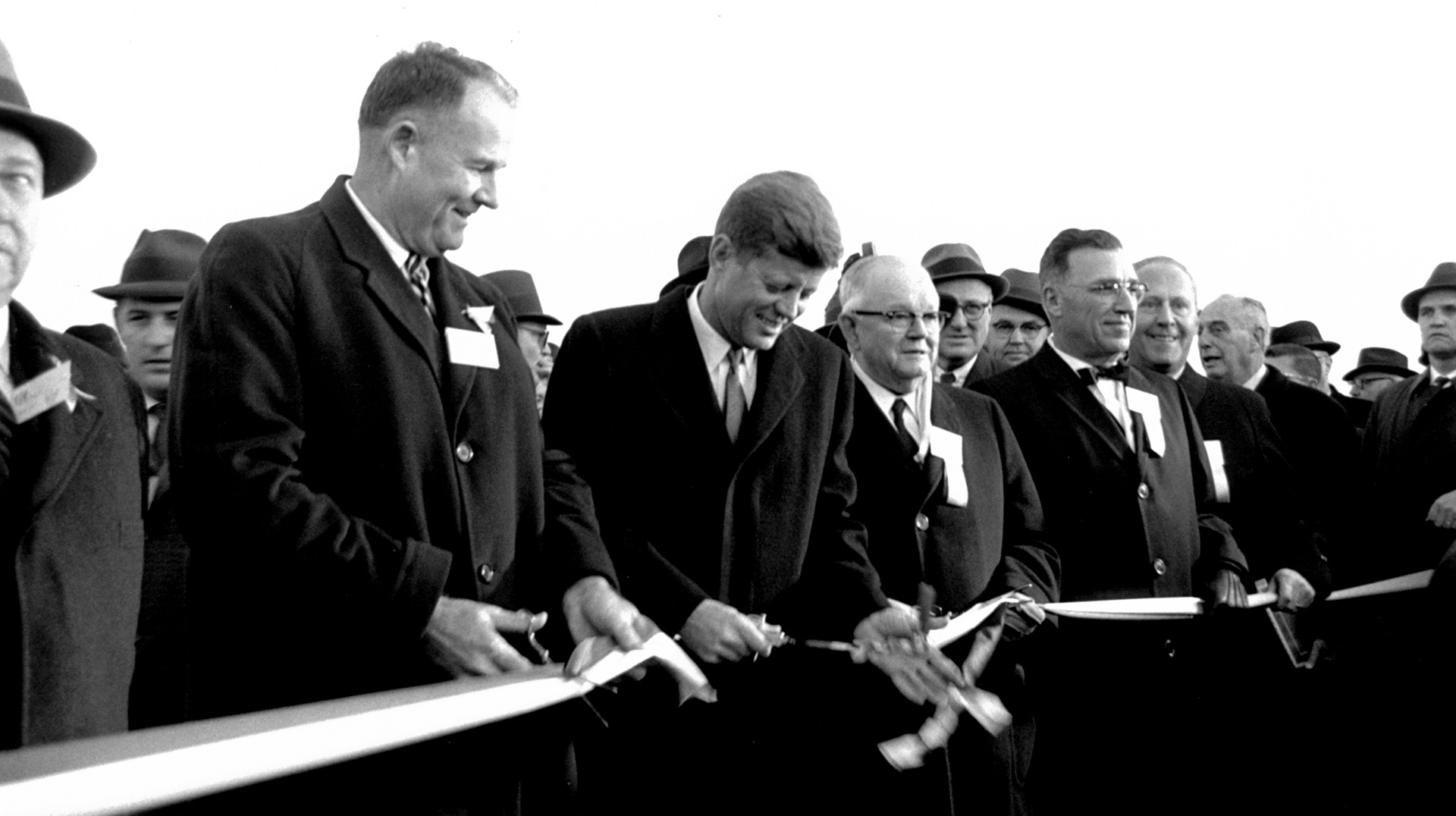 The Maryland Northern Expressway-Delaware Turnpike opened on November 14, 1963, with President John F. Kennedy helping to cut the ribbon before a crowd of 10,000. The new road, the President said, "symbolizes the effort we have made to achieve the most modern Interstate highway system in the world." Left to right: Governor Elbert N. Carvel of Delaware, President Kennedy, Governor J. Millard Tawes of Maryland, and John B. Funk, Chairman, Maryland State Roads Commission. (Photo courtesy John F. Kennedy Library)