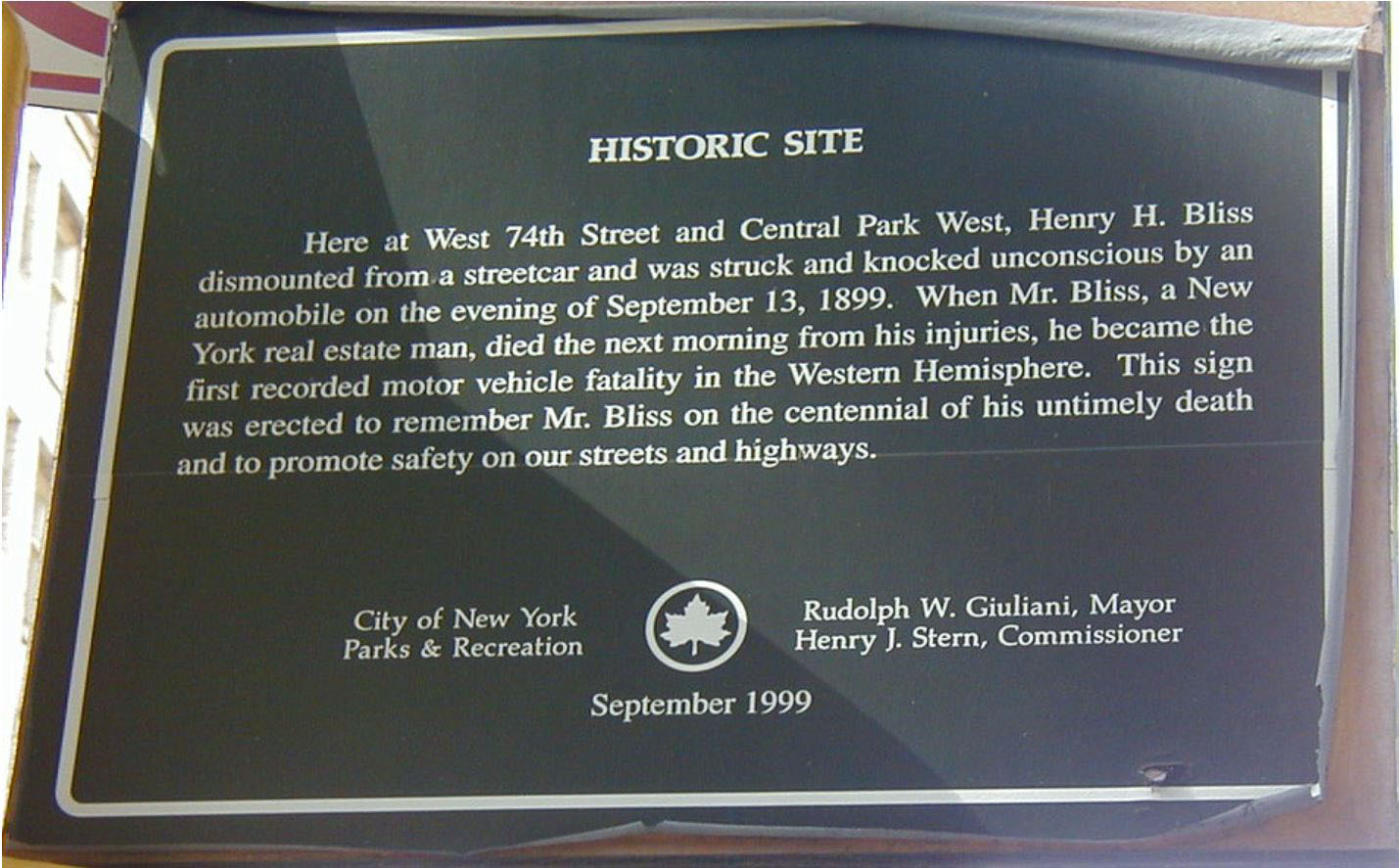 Photograph of the Hostoric plaque. It reads: Here at West 74th Street and Central Park West, Henry H. Bliss dismounted from a streetcar and was struck and knocked unconscious by an automobile on the evening of September 13, 1899. When Mr. Bliss, a New York real estate man, died the next morning from his injuries, he became the first recorded motor vehicle fatality in the Western Hemisphere. This sign was erected to remember Mr. Bliss on the centennial of his untimely death and to promote safety on our streets and highways.