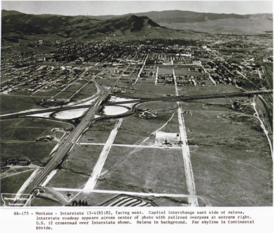 Montana - Interstate 15-4(6)182, facing west. Capitol interchange east side of Helena, with Interstate roadway appearing across center of photo with railroad overpass at extreme right. U.S. 12 crossroad over Interstate shown. Helena in background. Far skyline is Continental Divide.