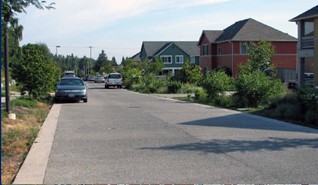 Street with housing on right side and parked car on left