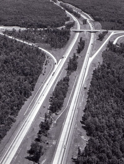 This section of Interstate highway (I-95 in Virginia) illustrates many of the safety features being built into the Interstate System, which will result in saving 8,000 lives each year when the system is complete. These features include: controlled access, wide median dividing opposing traffic, long sight distances, gentle curvatures, all crossings separated by bridges or underpasses, wide paved shoulders, and acceleration and deceleration lanes. Note also good design integrating esthetics and safety, including retention of trees in median and interchange area to reduce headlight glare, and adaptation of all highway elements to geographical features.