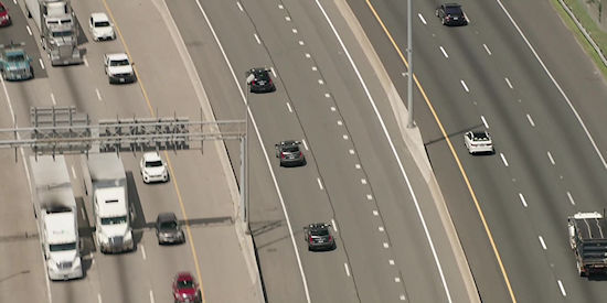 Figure 3. CARMA Cooperative Vehicles Test on Highway. The image shows a live highway with lanes going in three directions. From left to right, the first lane has cars and trucks driving southbound. The middle lane shows three CARMA vehicles testing the platooning application at even distances, they are heading northbound. The farthest right lane shows cars traveling north. 